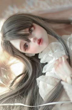 a close up of a doll with long gray hair wearing a white dress and posing for the camera