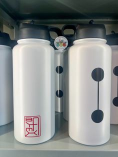 three white water bottles sitting on top of a shelf next to each other with black lids