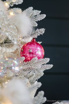 a pink ornament hanging from the top of a white christmas tree