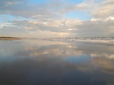 the sky is reflected in the wet sand at the beach