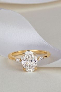 a yellow gold engagement ring with an oval cut diamond in the center on a white satin background