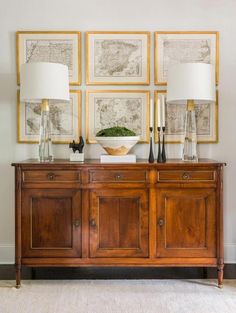 a wooden buffet with two lamps and pictures on the wall