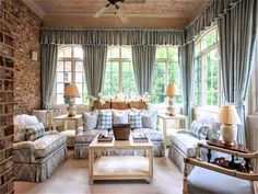 a living room filled with lots of furniture next to two large windows covered in blue and white curtains