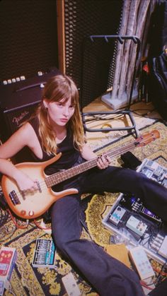 a woman sitting on the floor with a guitar in front of her and an amplifier behind her