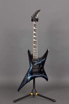 a black electric guitar on a stand against a gray background, with the top part of it's neck visible