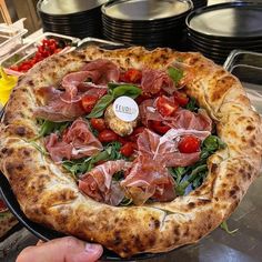 a pizza with ham, tomatoes and spinach on it in a restaurant kitchen setting