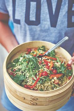 a person holding a wooden bowl filled with rice and vegtables in it