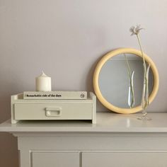 a white dresser with a mirror, vase and candle sitting on it's side