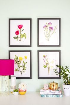 three framed flowers are on the wall above a white desk with a pink lamp and some books