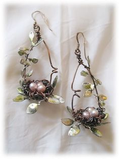 two pairs of earrings with leaves and pearls on them, hanging from hooks in front of a white sheet