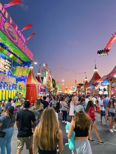 many people are walking around in an amusement park at night with lights and carnival rides