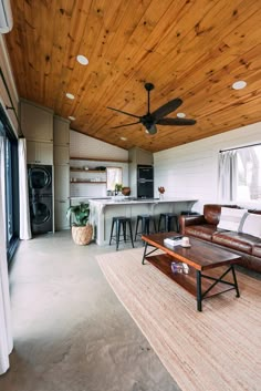 a living room filled with furniture next to a kitchen and an open floor plan on top of a wooden ceiling