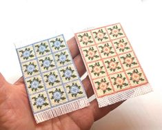 two cross stitch coasters sitting on top of each other in someone's hand