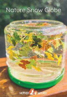 a jar filled with water and leaves on top of a wooden table next to trees