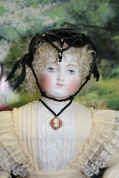 an old doll with curly hair wearing a white dress and black headdress is shown