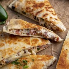 three quesadillas cut in half on a piece of parchment paper with jalapenos nearby