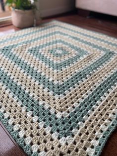 a crocheted rug on the floor with a potted plant in the background