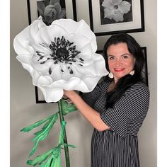 a woman holding a large white flower in front of two framed pictures on the wall