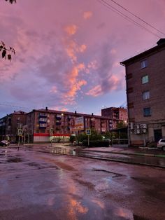 the sky is pink and purple as the sun goes down in an urban area with buildings on either side