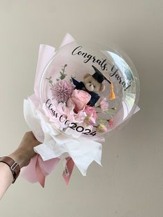 a hand holding a clear balloon with a teddy bear and flowers on it that says congrats you