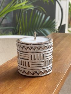 a white candle sitting on top of a wooden table next to a potted plant