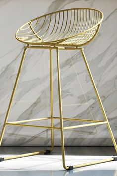 a golden metal bar stool against a marble wall