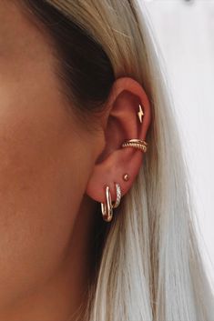 a woman with blonde hair wearing two gold ear cuffs and one silver earring that has an arrow on it