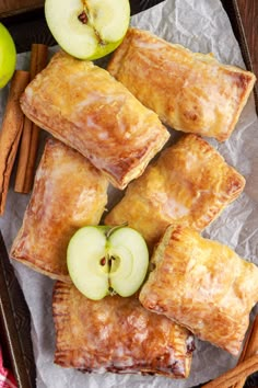 apple turnovers with cinnamon sticks and apples in the background on wax paper next to cinnamon sticks