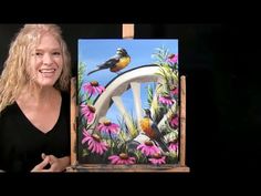 a woman standing next to an easel with a painting on it's side