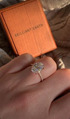 a woman's hand with a ring on it and an orange box in the background