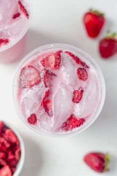 two cups filled with ice and strawberries on top of a white table next to bowls full of strawberries