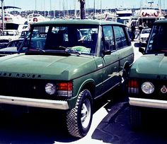 two green cars parked next to each other in a parking lot with lots of boats