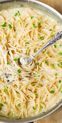 a bowl filled with pasta and peas on top of a wooden table next to a spoon