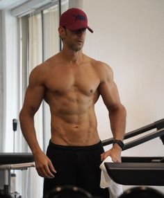 a shirtless man standing in front of a gym machine with his hands on his hips