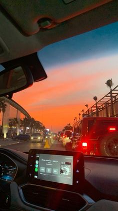 the sun is setting in an orange sky as cars drive down the road with palm trees on either side