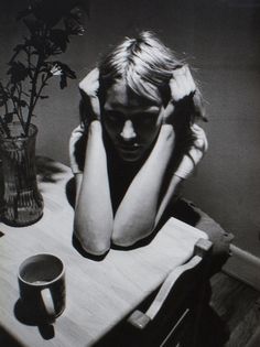 a black and white photo of a woman sitting at a table with her head in her hands