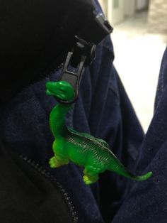 a green toy dinosaur in the pocket of someone's jeans