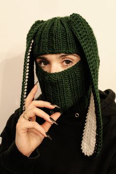 a woman wearing a green knitted mask and holding a cell phone to her face