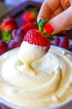 a hand dipping a strawberry into a bowl of cream