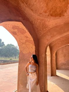 a woman standing in an archway with her hand on her hip and looking up at the sky