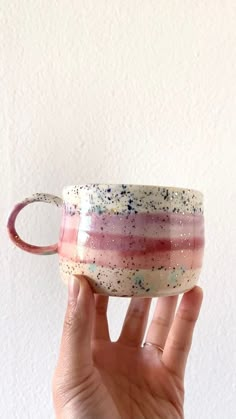 a hand holding a coffee cup with pink, blue and white speckles on it