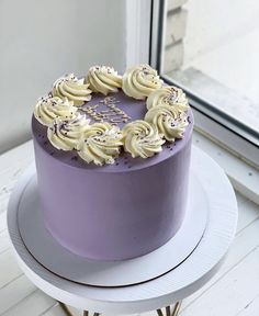 a purple cake sitting on top of a white table next to a window with frosting and sprinkles