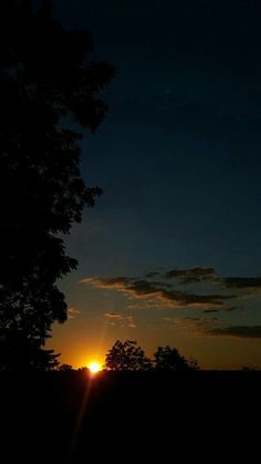 the sun is setting behind some trees in the dark sky with no one around it