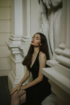 a woman in a black dress sitting on the ground next to a white statue with her eyes closed