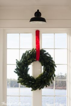 a wreath hanging on the front door of a house with a red ribbon around it