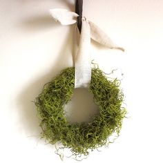 a green wreath hanging on the wall with a white cloth tied to it and a black twig sticking out of it