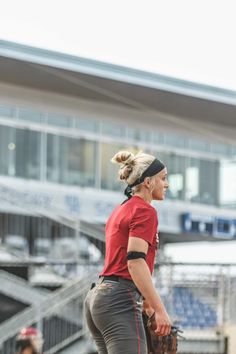 a woman in red shirt and black pants holding a catchers mitt