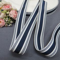 a blue and white striped ribbon next to some flowers on a gray table with a plate in the background