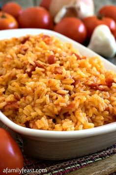 a white bowl filled with rice next to tomatoes and garlic on top of a table