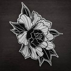 a black and white flower with leaves on it's back side, sitting on a wooden surface